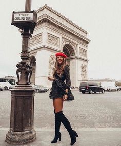 a woman standing in front of the arc de trioe with her legs crossed and wearing thigh high boots