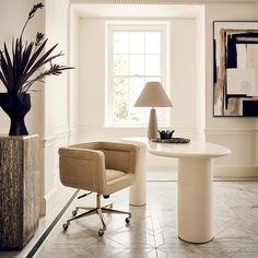 a room with a table, chair and lamp in the corner near a potted plant