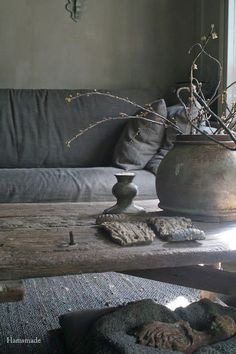 a vase sitting on top of a wooden table next to a gray couch and pillows