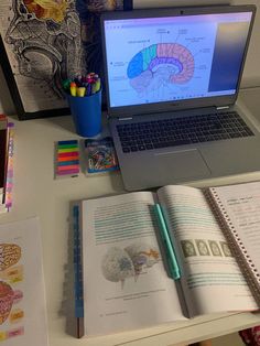 an open laptop computer sitting on top of a desk next to a notebook and pencils