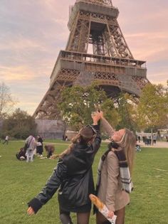 two women standing in front of the eiffel tower, reaching up for something