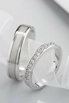 two white gold wedding bands with diamonds on them, sitting next to each other in front of a napkin