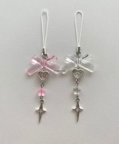 two pairs of earrings with bows and hearts hanging from hooks on a white surface,