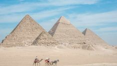 three people riding camels in front of the pyramids