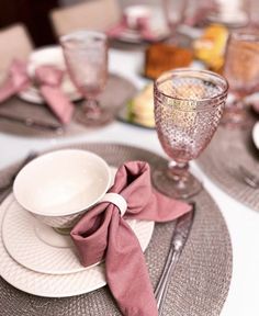 the table is set with dishes, silverware and pink napkins