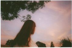 a woman standing under a tree looking up at the sky with clouds in the background