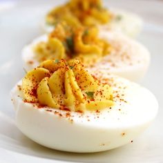 three deviled eggs with sprinkles and seasoning sit on a white plate