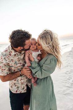 a man and woman holding a baby on the beach with their arms around each other