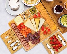 a variety of cheeses, fruits and meats on wooden serving trays with utensils