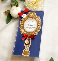 a blue and gold wedding card with a red ribbon around the edge on a white tablecloth