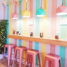 three pink stools in front of a colorful striped wall with lights hanging from the ceiling