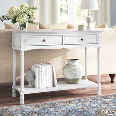 a white console table with two drawers and books on the bottom shelf next to a couch