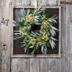 a wreath hanging on the side of a wooden door with green leaves and yellow flowers