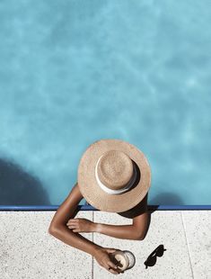 a woman in a hat sitting on the edge of a swimming pool