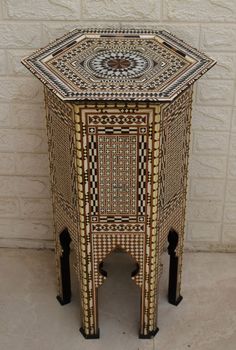 an intricately designed side table sits against a white brick wall