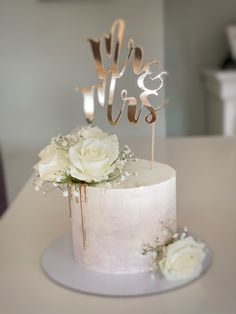 a wedding cake with white flowers and the words we & us on top is sitting on a table