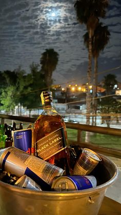 a metal bucket filled with bottles and cans on top of a wooden table under a full moon