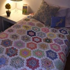 a bed with a colorful quilt on top of it next to a night stand and lamp