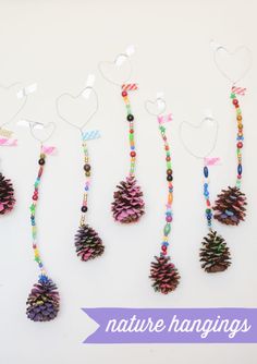 five pine cones are hanging from strings on a white surface, with hearts and ribbons attached to them