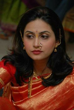 a woman in a red sari with gold jewelry on her face and nose piercings