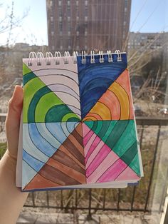 a hand holding up a spiral notebook with colored papers on it in front of a cityscape