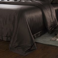 a bed with brown sheets and pillows on top of a wooden floor next to a rug