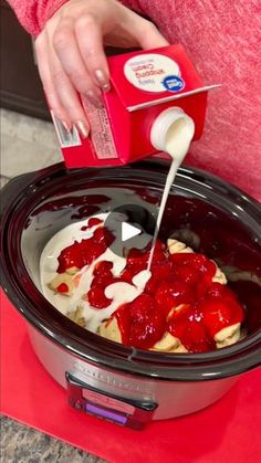 someone pouring cream into a crock pot with strawberries on top and yogurt in it