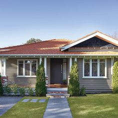 a gray house with red roof and white trim on the front door is surrounded by greenery