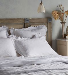 a bed with white linens and ruffled pillows on it's headboard