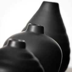 three black vases sitting side by side on a white surface, one is empty