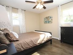 a bed room with a neatly made bed and a ceiling fan on the side of it