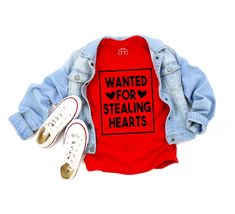 a red shirt with the words wanted for stealing hearts on it next to white shoes