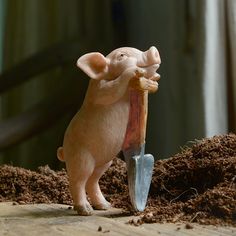 a toy pig holding a shovel on top of dirt