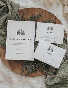 three wedding stationery cards on a wooden platter with pine branches and greenery