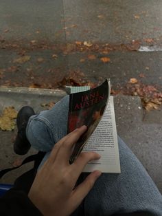 a person sitting down reading a book on the sidewalk with their feet up in the air