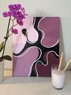 a vase with some purple flowers next to a painting