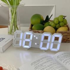 an alarm clock sitting on top of a table next to a book and some fruit