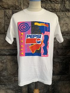 a white pepsi t - shirt is on a mannequin stand in front of a stone wall