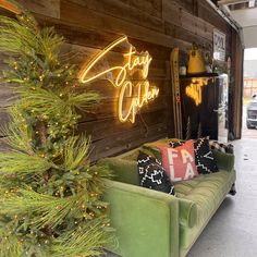 a green couch sitting next to a christmas tree in front of a wooden wall with neon signs on it