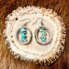 a pair of earrings sitting on top of a piece of wood next to a fur