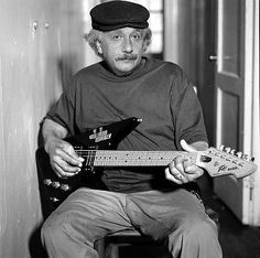 an old man sitting in a chair holding a guitar and looking at the camera while wearing a hat