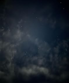 the night sky is dark and cloudy with stars in the clouds, as seen from below