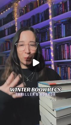 a woman standing in front of a bookshelf holding her hand out to the camera