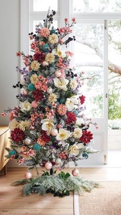 a decorated christmas tree in front of a window with white and red flowers on it