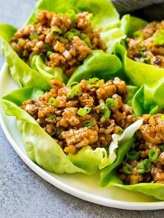 lettuce wraps filled with meat and green onions on a white plate, ready to be eaten