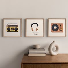 three framed art pieces hang on the wall above a dresser with books and a vase