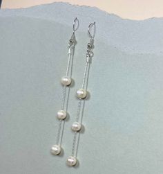 These freshwater pearl dangle drop earrings are a stunning choice for any bride or anyone who loves classic elegance. Handcrafted with sterling silver, they feature lustrous freshwater pearls that are carefully selected for their beauty and quality. The pearls dangle delicately from the silver hooks, creating a timeless and romantic look. These earrings are perfect for a wedding or any special occasion where you want to add a touch of refinement to your outfit. The long length of the earrings ad Dangly Pearl Earrings Silver, Classic White Drop Chandelier Earrings, Elegant Drop Pearl Earrings, Pearl White Chandelier Earrings With Pearl Drop For Anniversary, Classic White Pearl Drop Chandelier Earrings, Pearl White Pearl Drop Chandelier Earrings For Anniversary, Pearl White Chandelier Earrings For Anniversary, Pearl Drop Dangle Linear Earrings, Elegant Nickel-free Linear Earrings For Wedding