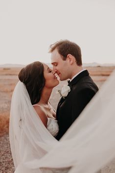 a bride and groom kissing in the desert with their veil blowing around them as they look into each other's eyes