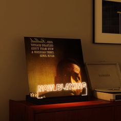 an illuminated sign on top of a wooden table next to a record player and laptop