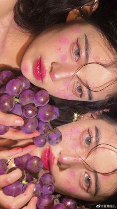 two young women holding grapes in their hands and looking at the camera while laying down